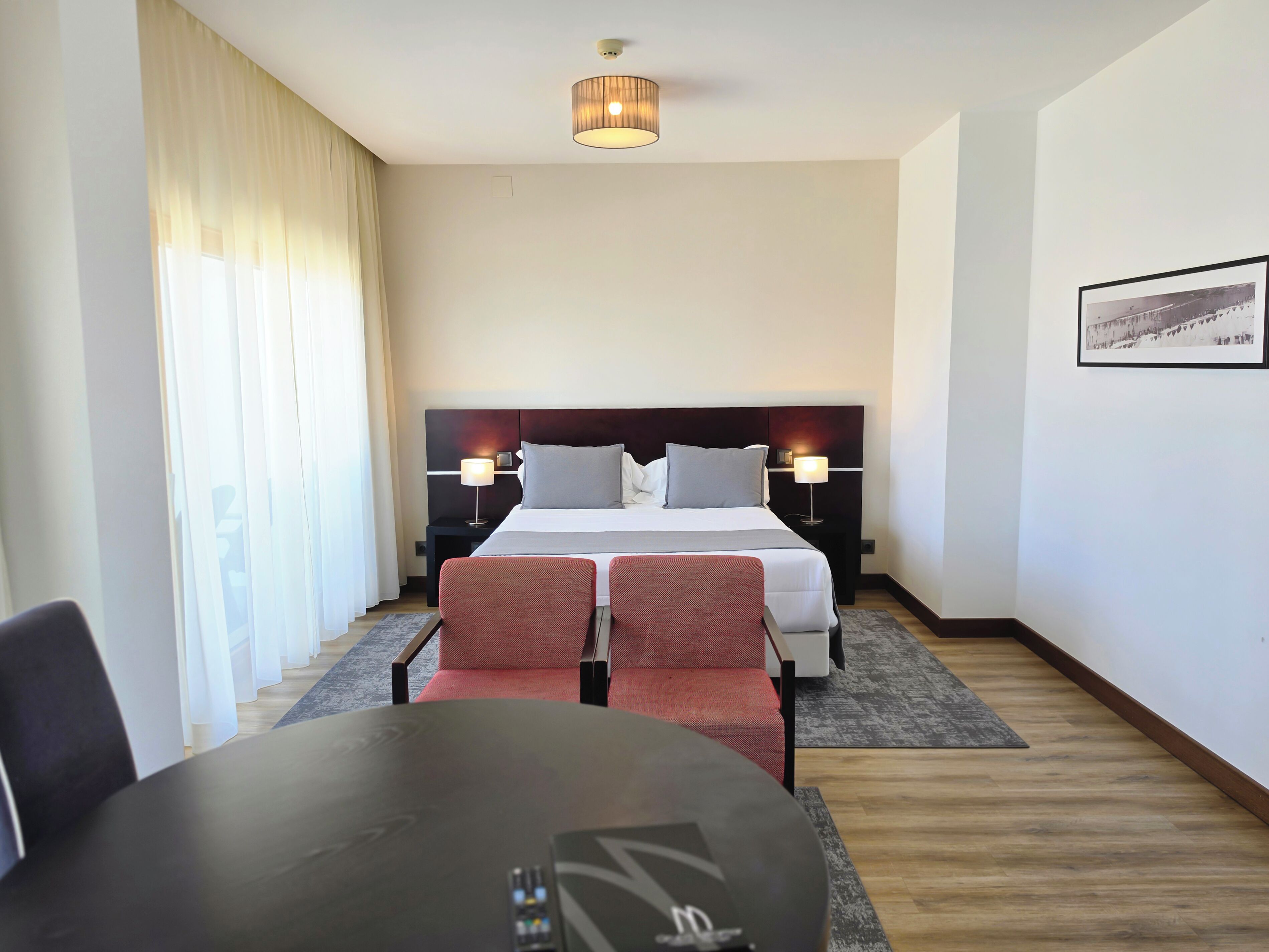 Une chambre d’hôtel comprenant un lit, deux tables de chevet, un bureau, une chaise et un luminaire au plafond.