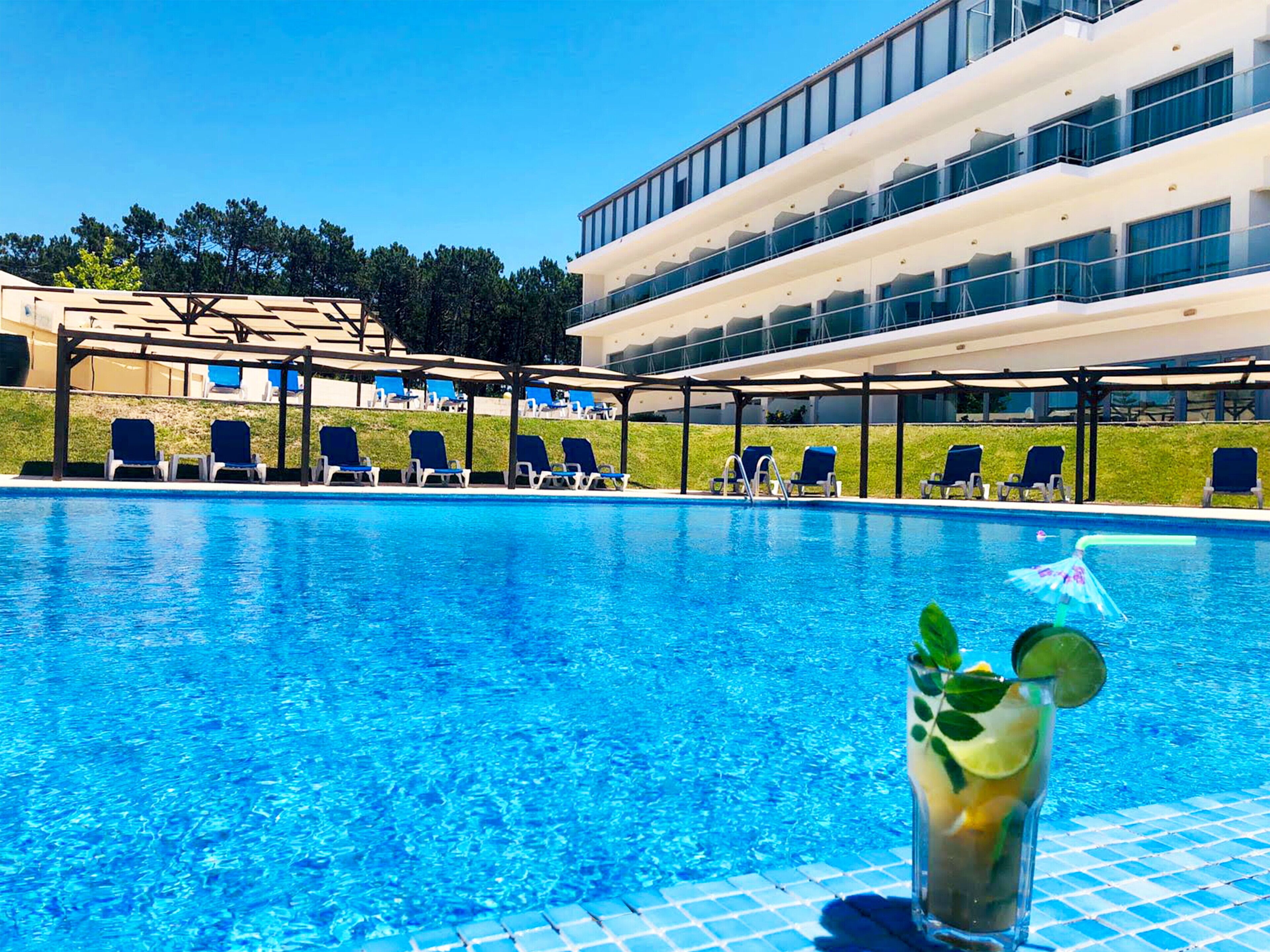 A swimming pool with lounge chairs and a glass of drink.