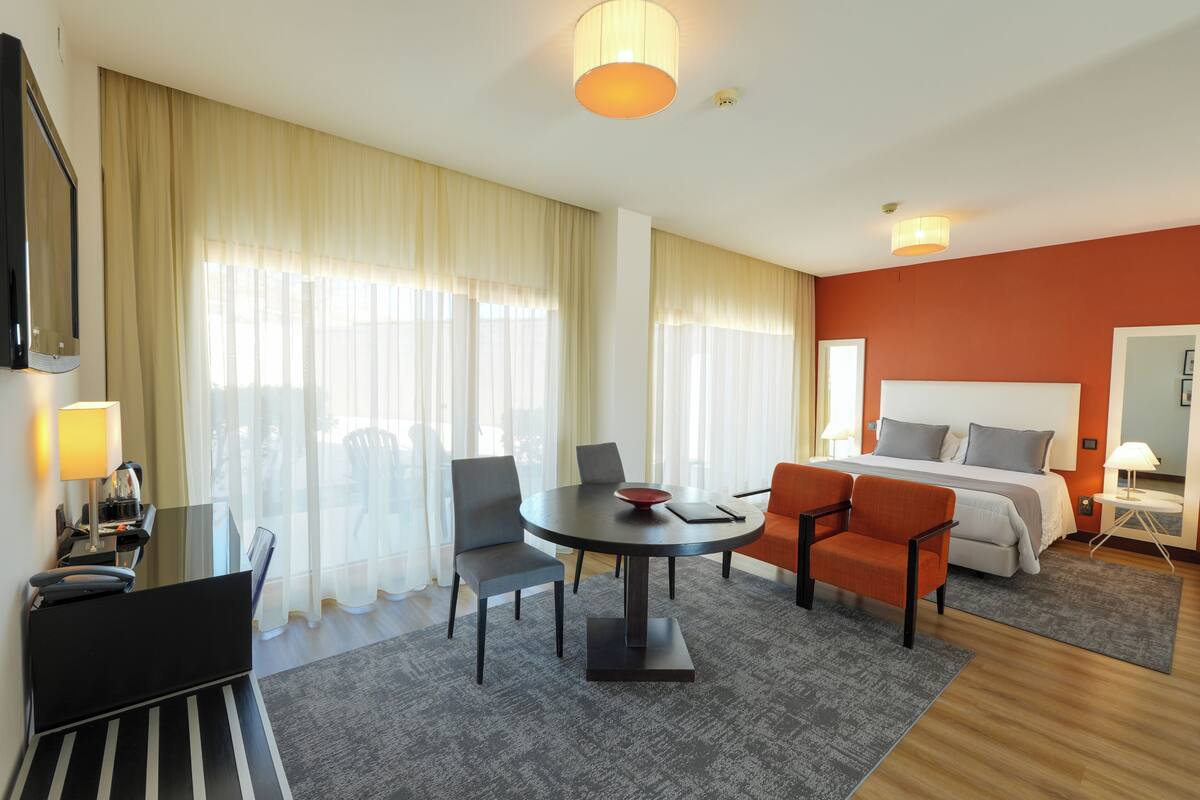 A hotel room with a bed, a desk, a chair, a table, and a TV.