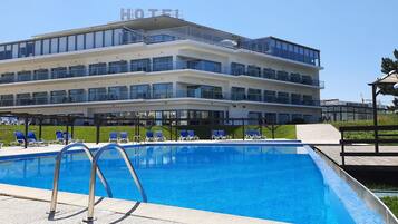 A hotel with a swimming pool, multiple balconies, and a clear sky.