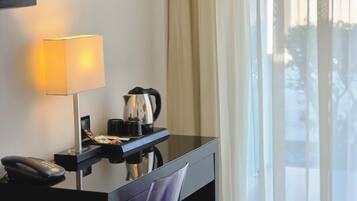 Habitación de hotel con escritorio, lámpara, cafetera y teléfono.
