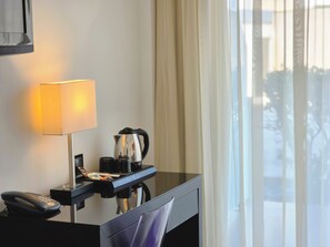 A hotel room with a desk, a lamp, a coffee maker, and a telephone.