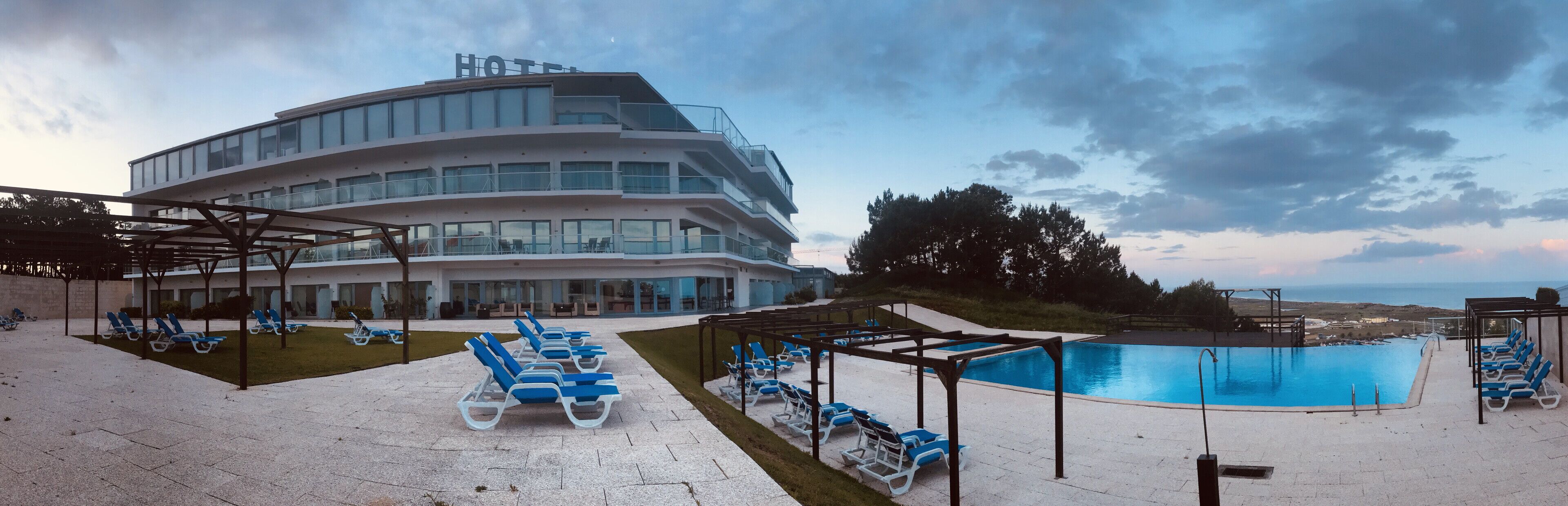 Un hotel moderno con zona de piscina, sillones de descanso y vistas al mar.
