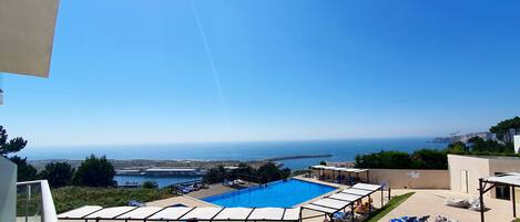 A pool area with sun loungers and a view of the sea.