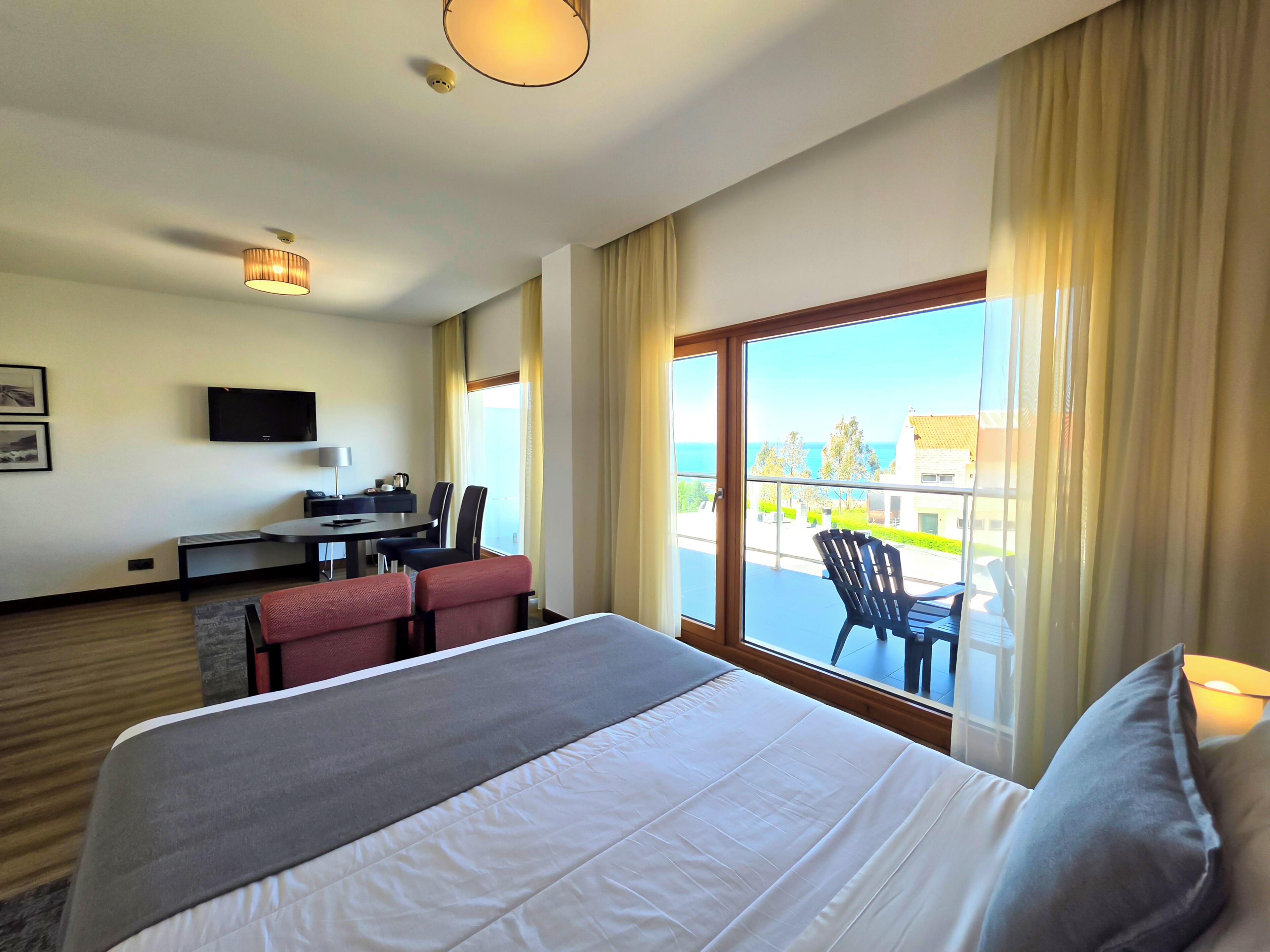 Ein Hotelzimmer mit Bett, Schreibtisch mit Stuhl, Fernseher und einem Balkon mit Blick.