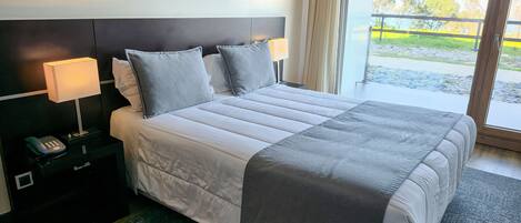 Habitación de hotel con una cama grande, lámparas de noche, un teléfono en la mesita y vistas al exterior.