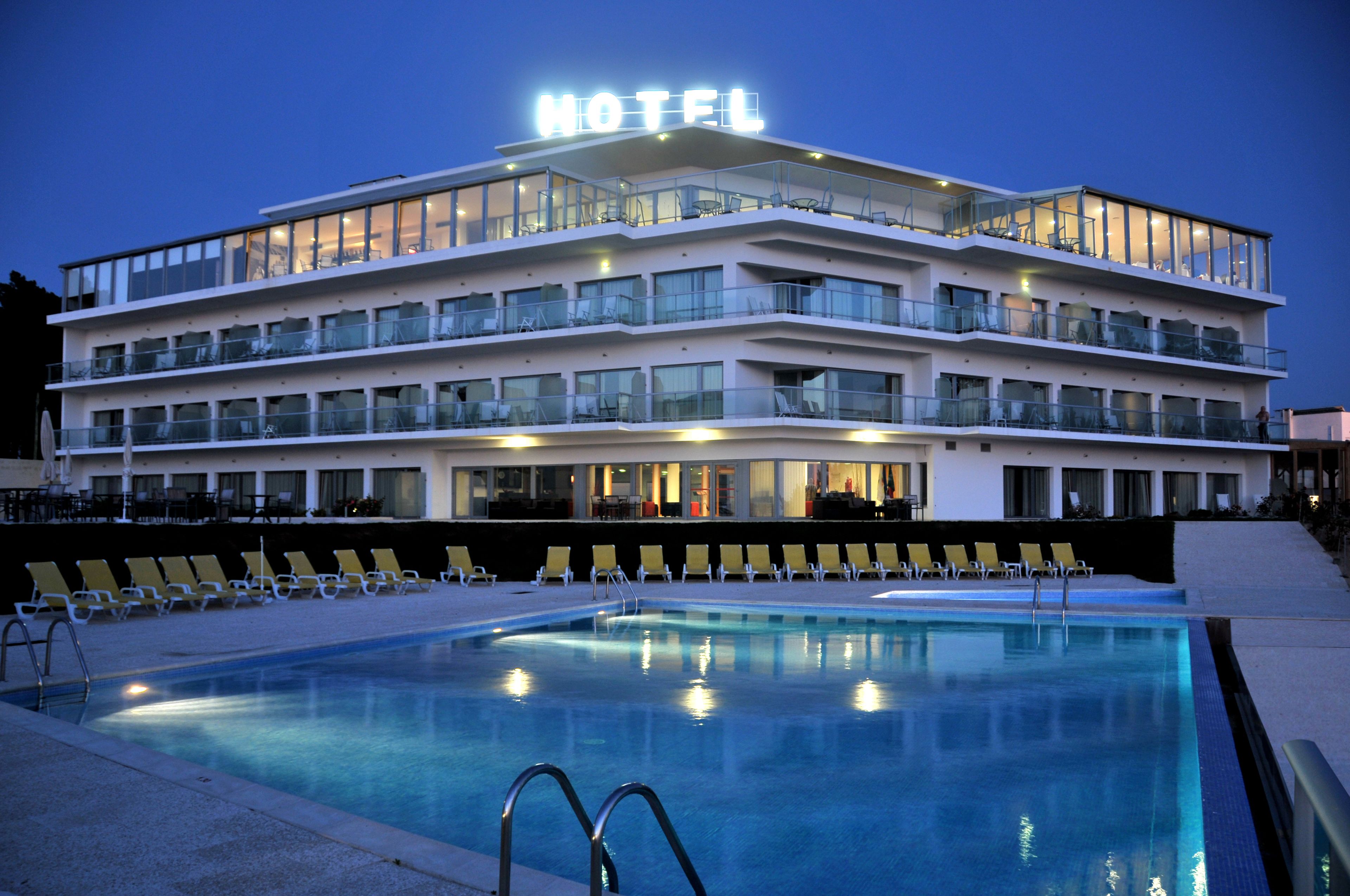 Ein mehrstöckiges Hotel mit Schwimmbad, Außenbereich zum Sitzen und einem Balkon mit Glasgeländern.