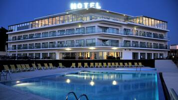 Ein mehrstöckiges Hotel mit Schwimmbad, Außenbereich zum Sitzen und einem Balkon mit Glasgeländern.