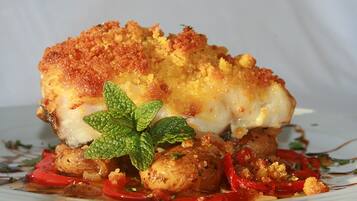 Un plato con costra dorada, salsa blanca y pimientos rojos, adornado con una hoja de menta.