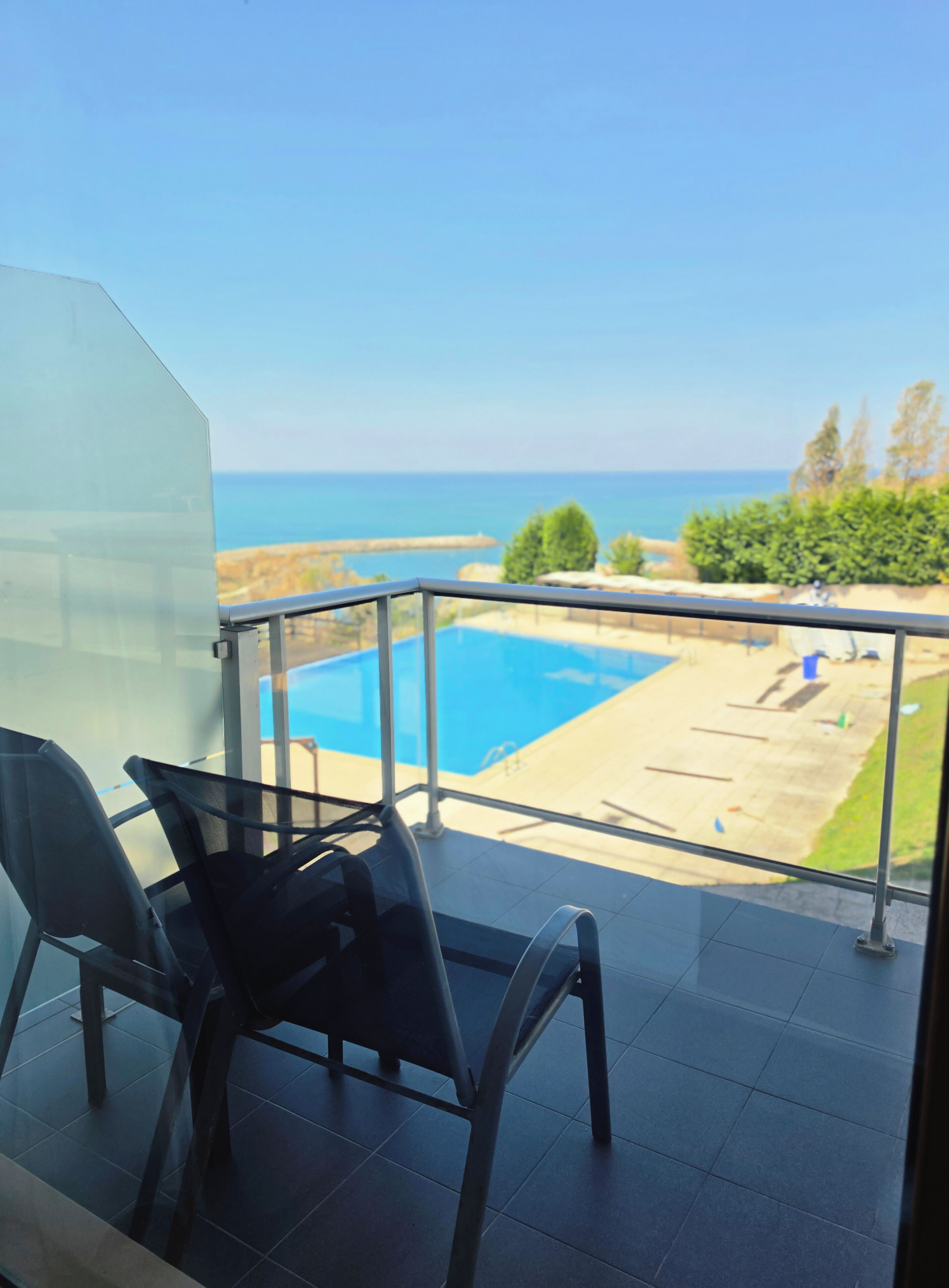 A balcony with a view of a swimming pool and the sea.