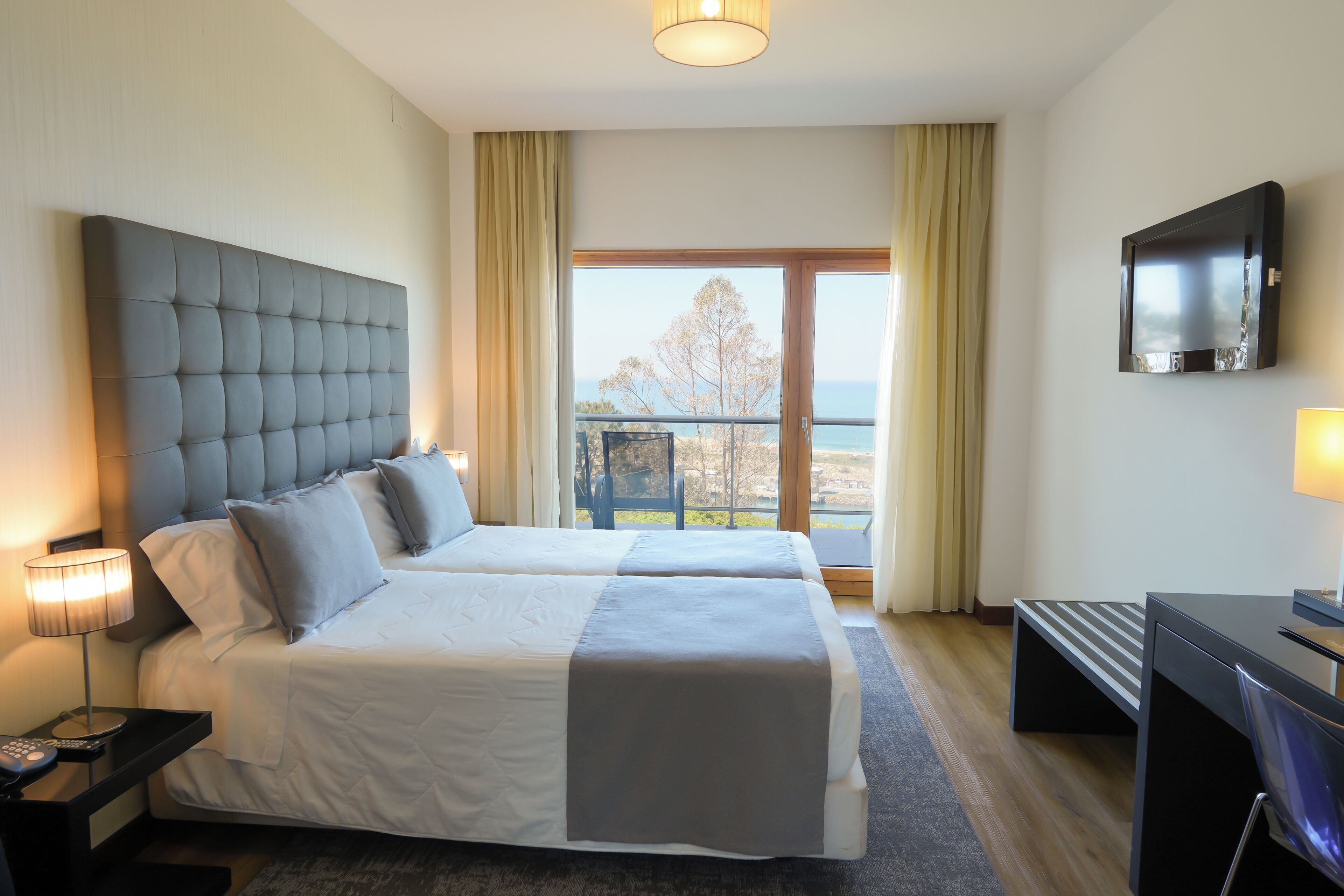A hotel room with two beds, a TV, a desk, and a view of the outdoors.