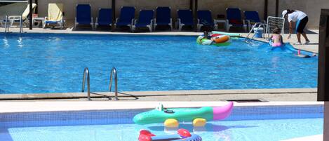 A swimming pool with blue water, a diving board, and several lounge chairs.