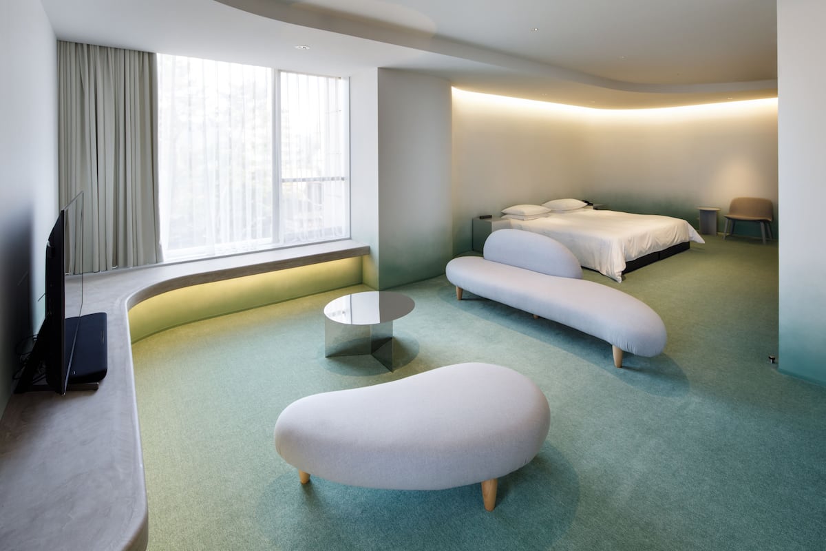 Une chambre d’hôtel moderne au design épuré, avec un lit, un canapé, une table basse ronde et un téléviseur.