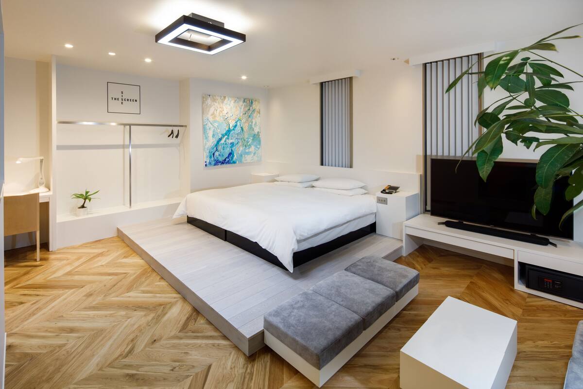 Une chambre moderne avec un lit, une télévision, une plante et une grande fenêtre.