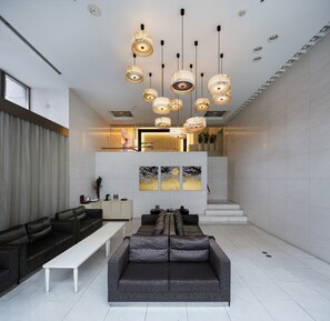 Una sala de estar moderna con un sofá de color oscuro y estampado, un banco blanco y múltiples lámparas colgantes.