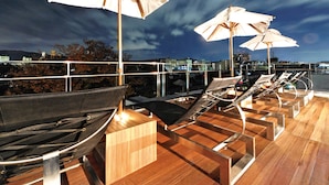 A rooftop terrace with lounge chairs and umbrellas, overlooking a cityscape at night. - The Screen (Kyoto)