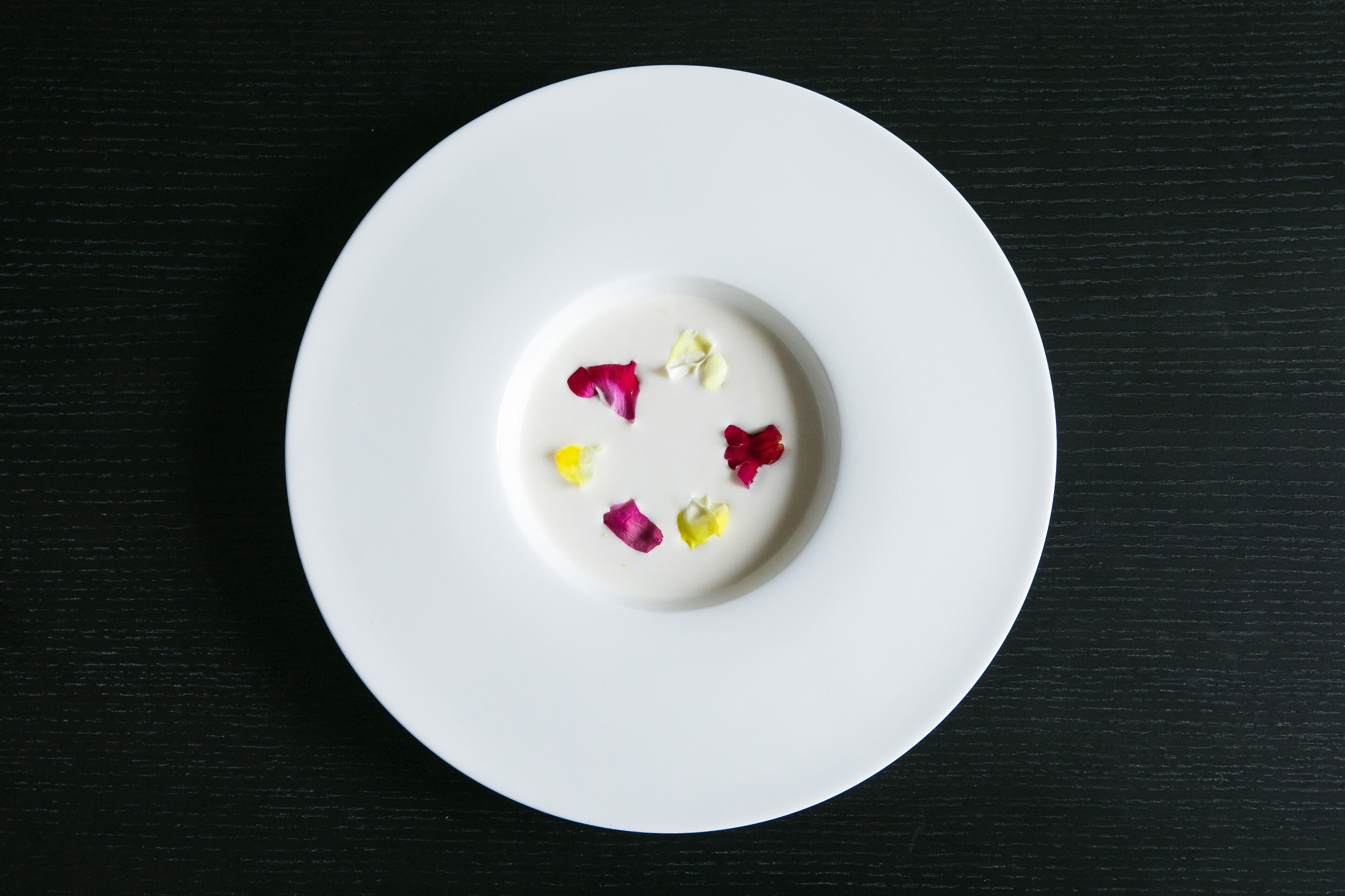 A white plate with a white substance and colorful flower petals on a black surface.