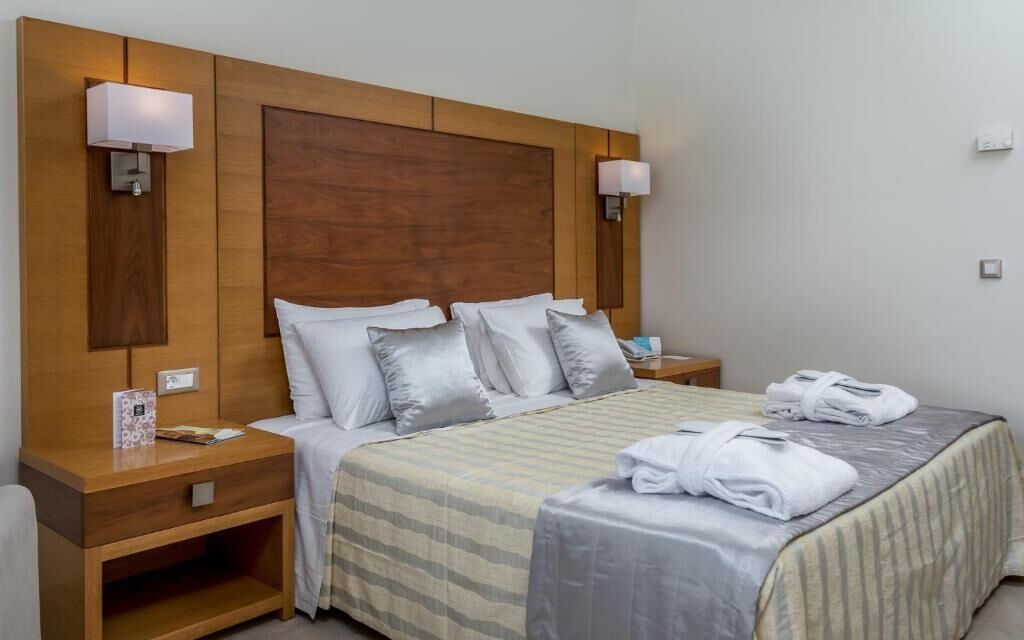 Une chambre d’hôtel avec un grand lit, une tête de lit en bois, deux tables de chevet et deux lampes fixées au mur.