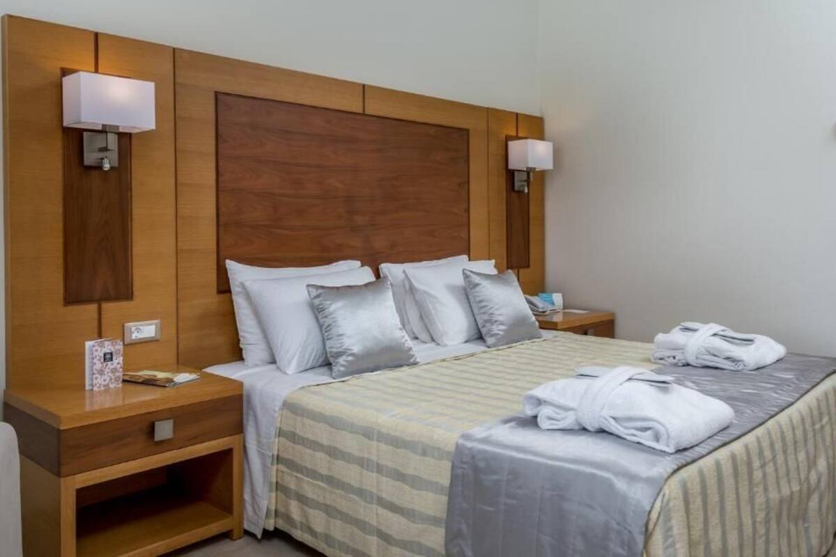Une chambre d’hôtel avec un grand lit, une tête de lit en bois, deux tables de chevet et deux lampes fixées au mur.