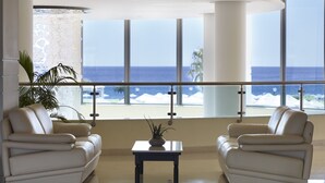 A modern living room with two white leather sofas, a small table, and a view of the ocean through large windows. - Apollo Blue (Rhodes)