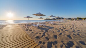 A beach with a wooden walkway, sun umbrellas, and lounge chairs. - Apollo Blue (Rhodes)