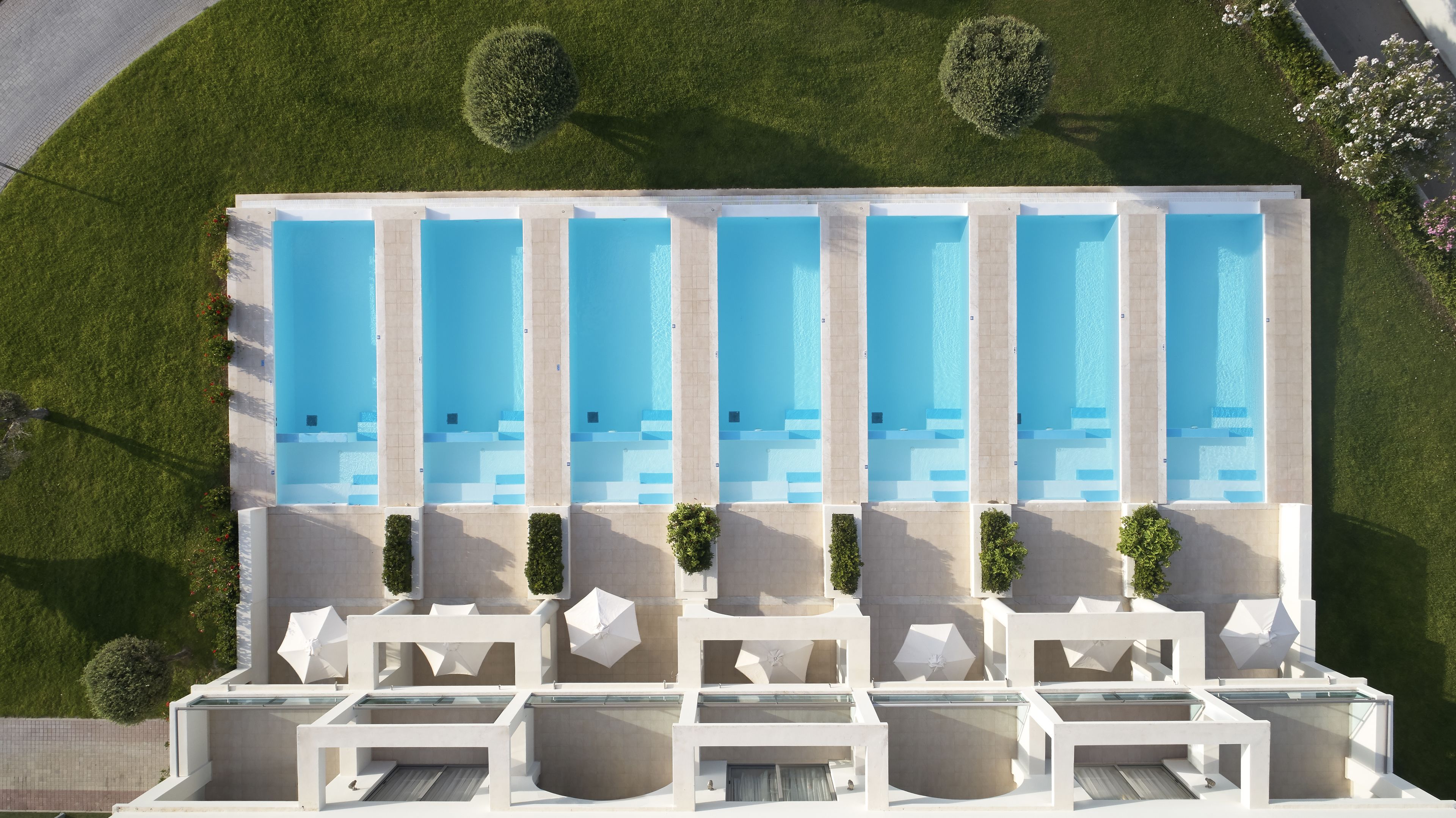 Un hotel moderno con piscina en la azotea, varias piscinas y tumbonas.