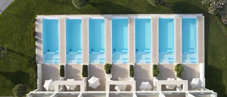 Un hotel moderno con piscina en la azotea, varias piscinas y tumbonas.