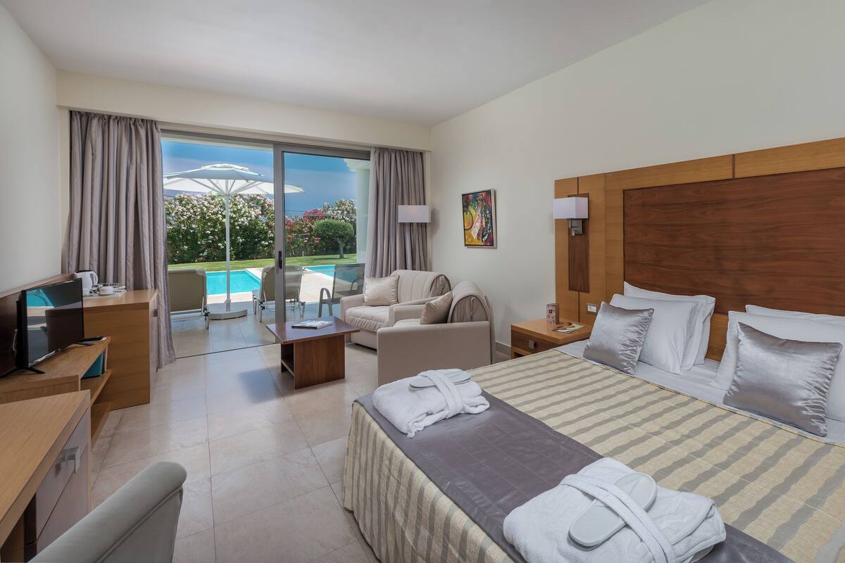 Une chambre d’hôtel avec un grand lit, un bureau, une télévision, un canapé, une table basse et une vue sur une piscine.