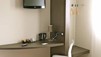 A hotel room with a bed, a desk with a TV, a chair, a coffee maker, and a trash bin.