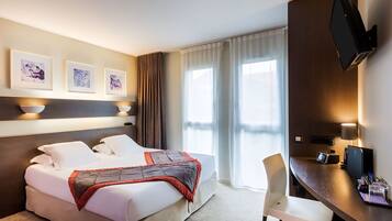 Une chambre d’hôtel équipée d’un lit, d’un bureau, d’une chaise, d’une télévision et décorée avec des œuvres d’art au mur.