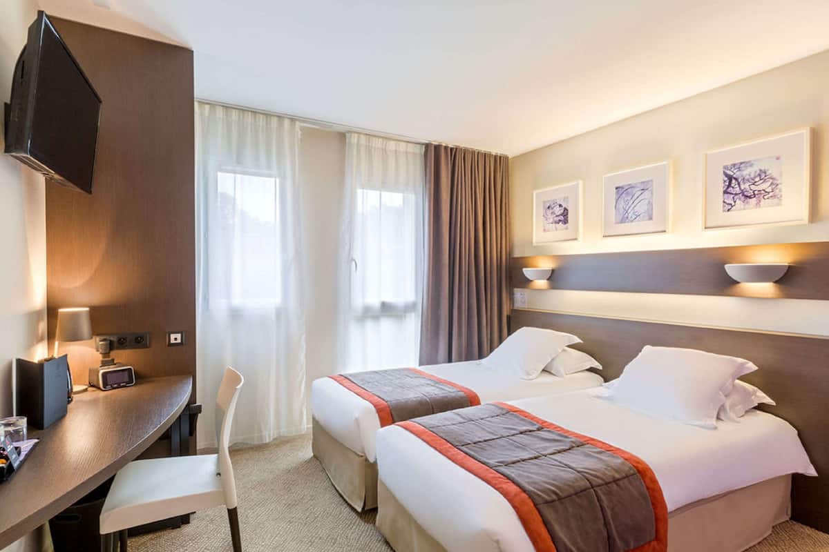 Une chambre d’hôtel avec deux lits, un bureau, une chaise, une télévision et des œuvres d’art accrochées au mur.