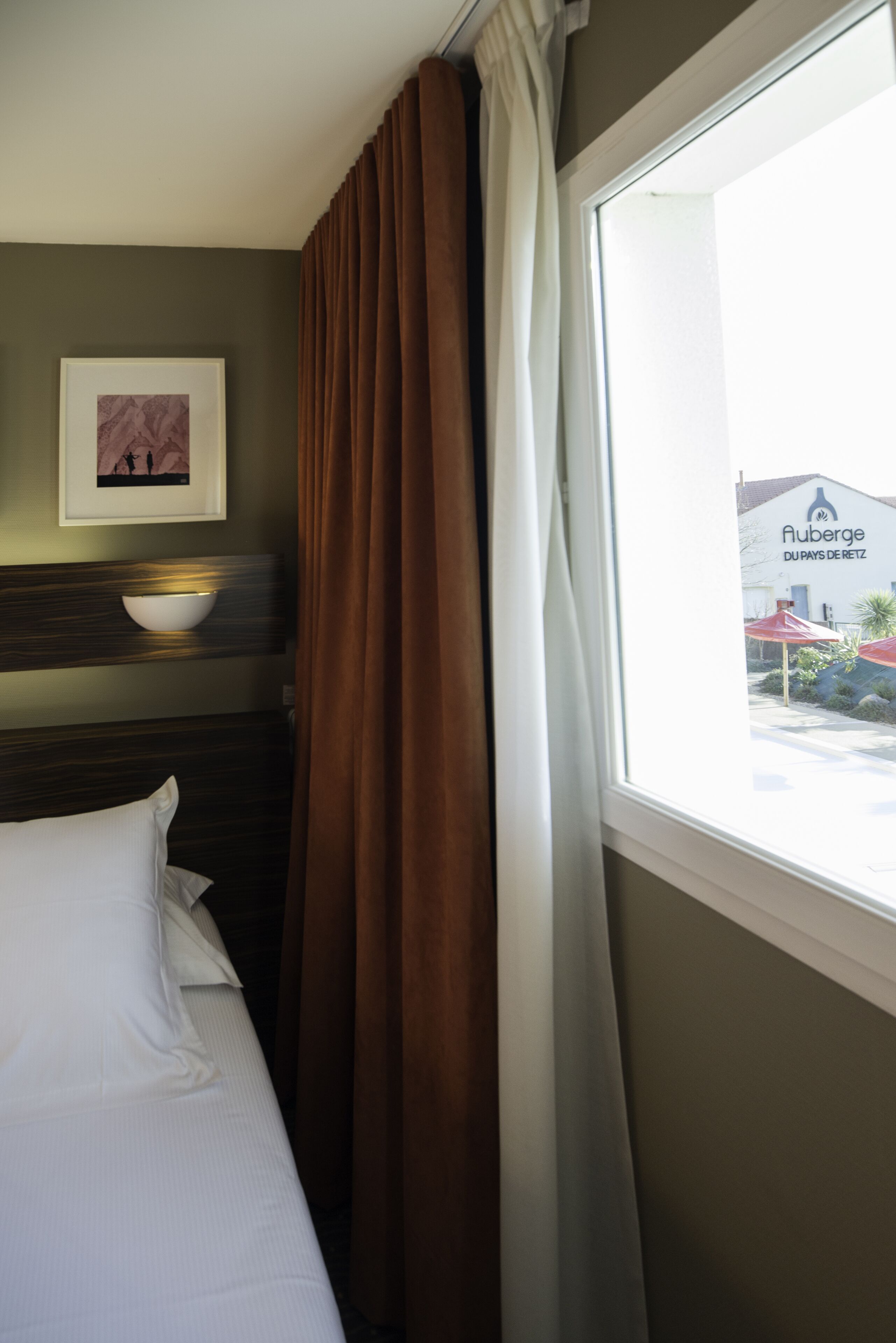 Quarto de hotel com uma cama, um quadro na parede e uma janela com cortinas.