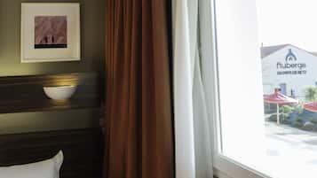 Quarto de hotel com uma cama, um quadro na parede e uma janela com cortinas.