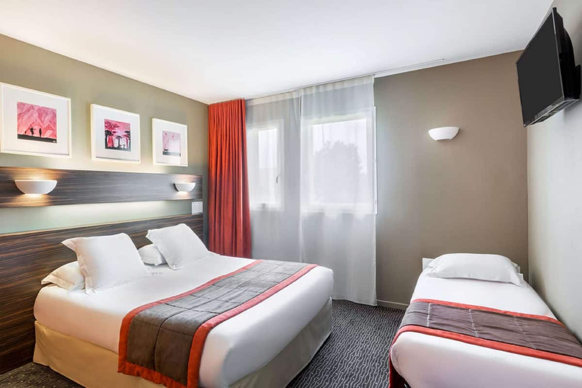 Une chambre d’hôtel avec un grand lit, un lit plus petit, une télévision, une fenêtre avec des rideaux et des œuvres d’art accrochées au mur.