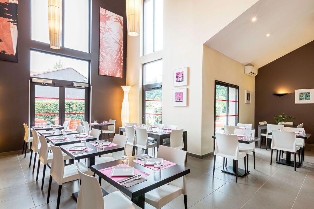 Zona pranzo con diversi tavoli e sedie, ampie finestre e opere d'arte alle pareti.
