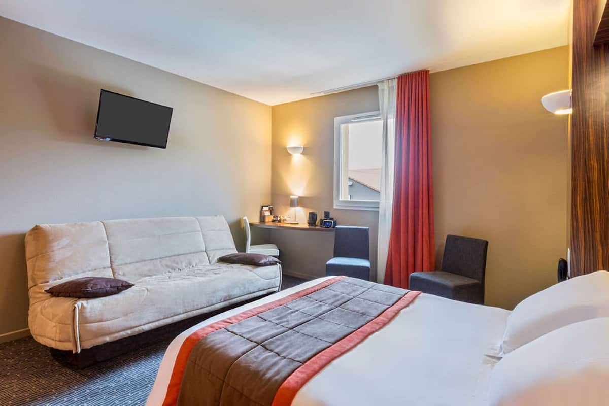 Une chambre d’hôtel comprenant un lit, un canapé, un bureau, une chaise, un téléviseur fixé au mur et une fenêtre avec des rideaux.