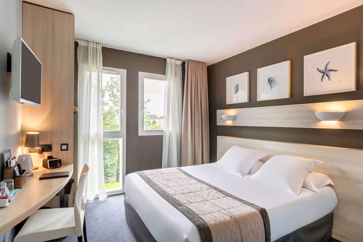 Une chambre d’hôtel équipée d’un lit, d’un bureau, d’une chaise, d’une télévision et d’œuvres d’art accrochées au mur.