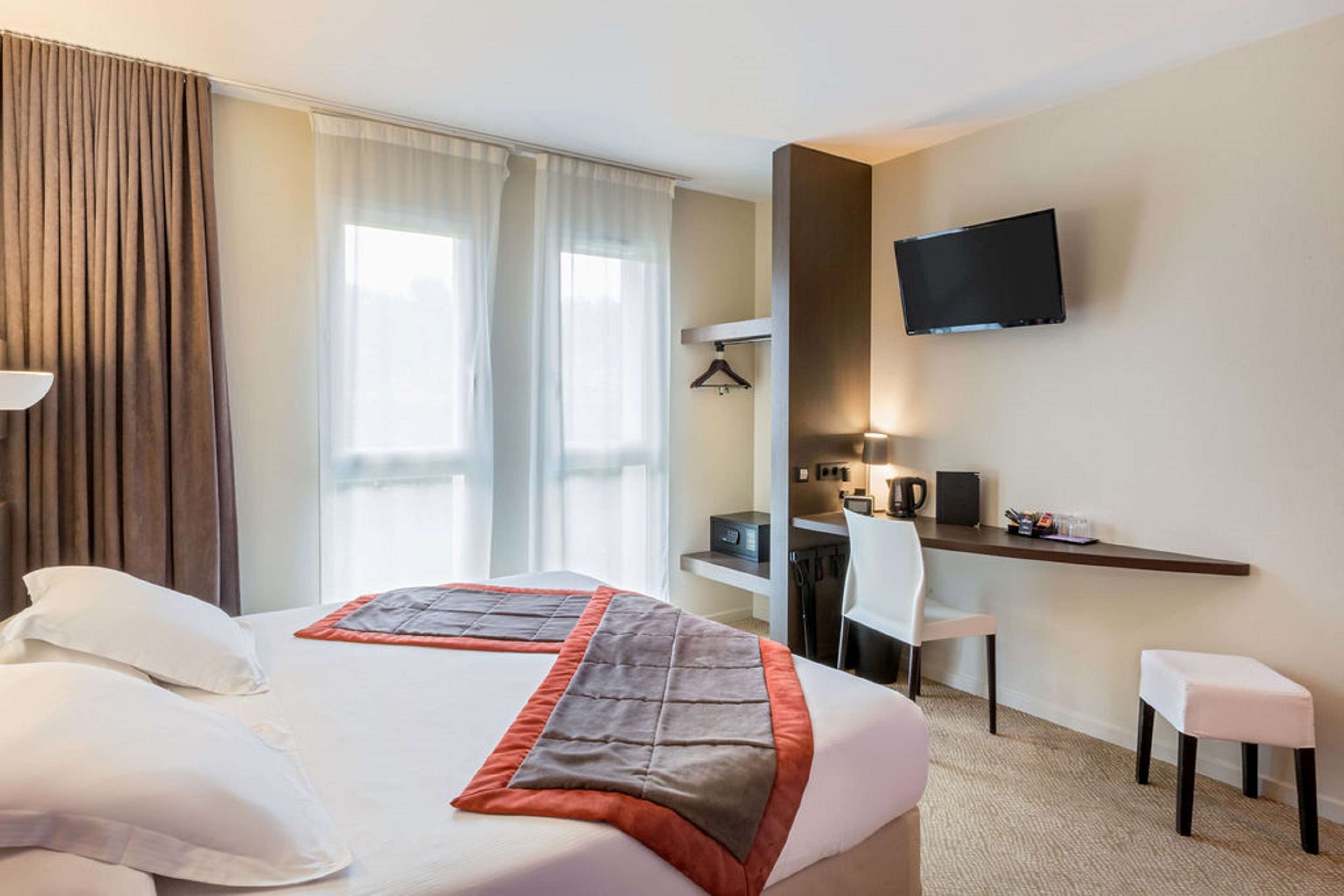 Una habitación de hotel con cama, escritorio, silla, televisión y una pequeña mesa.