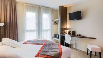 Una habitación de hotel con cama, escritorio, silla, televisión y una pequeña mesa.
