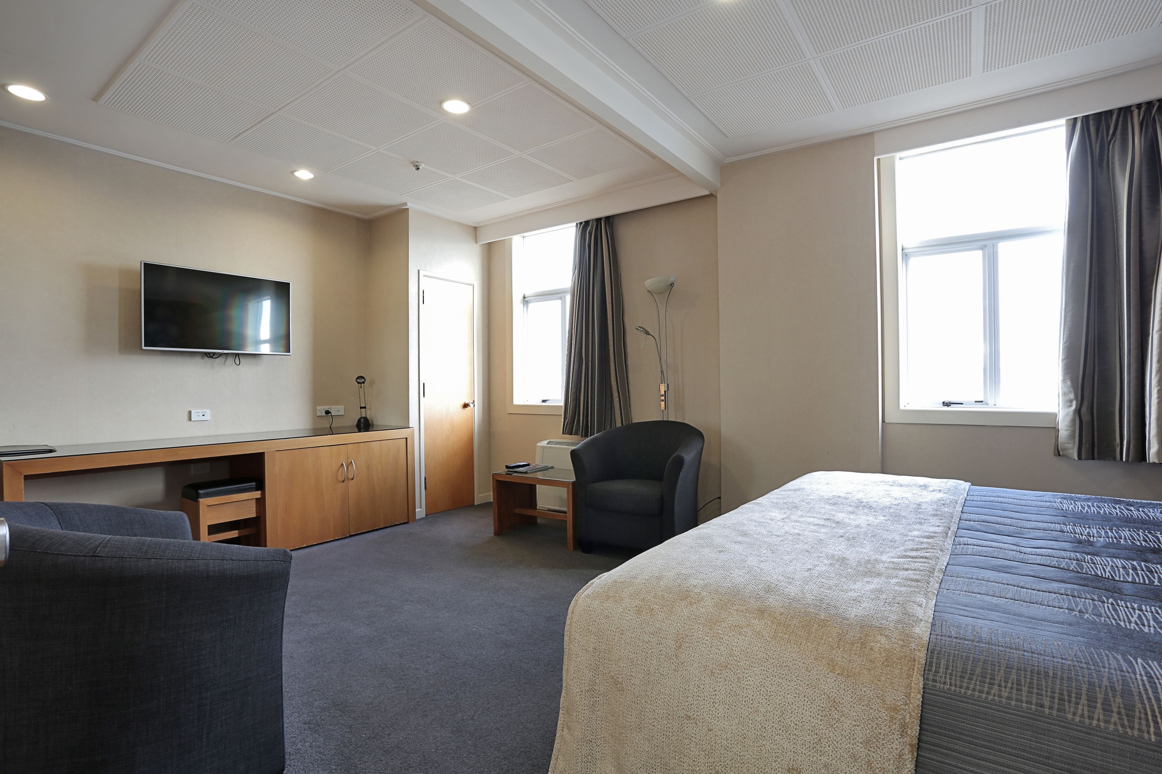 Een hotelkamer met een bed, bureau, stoel, tv aan de muur en een raam met gordijnen.