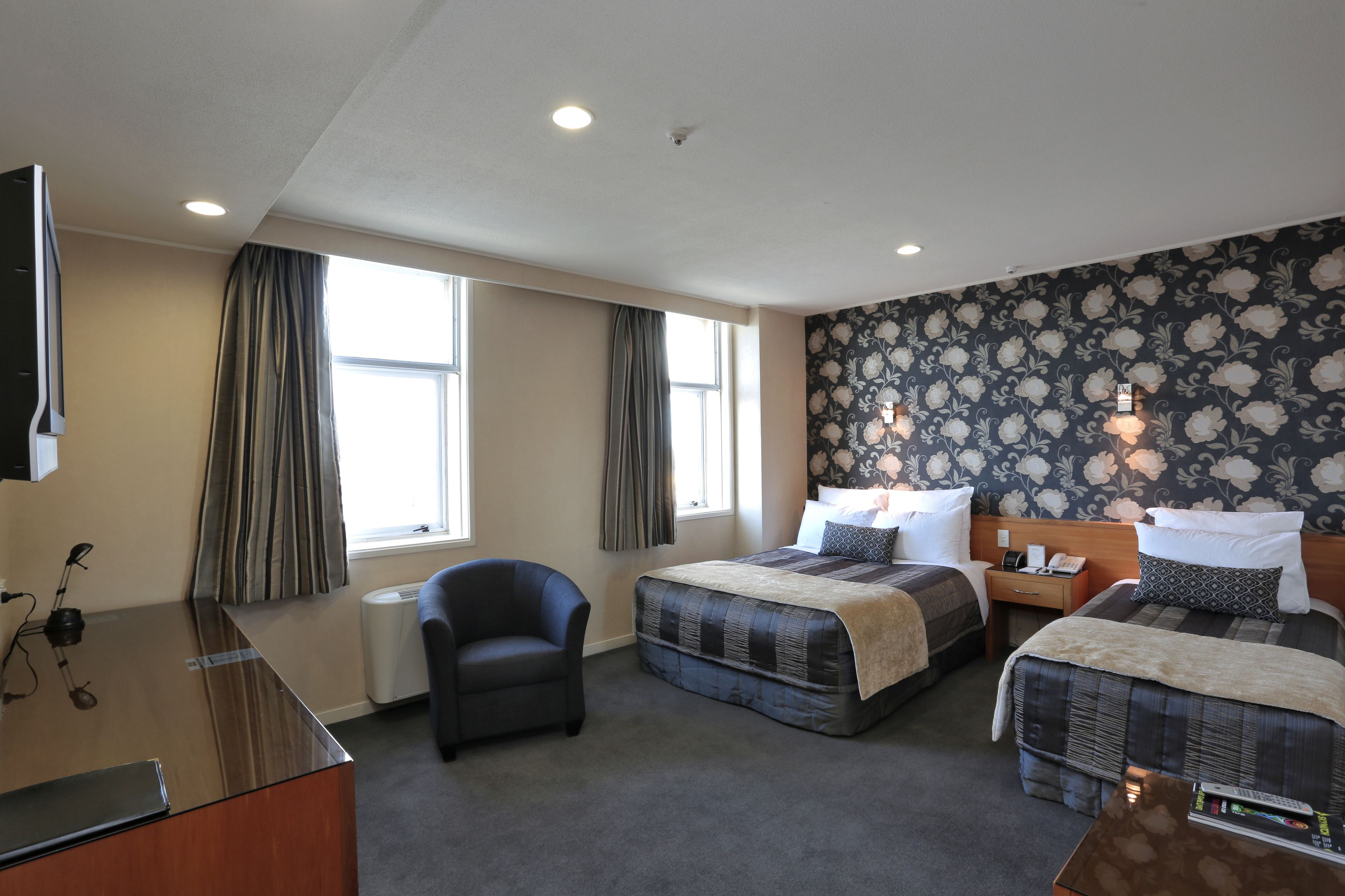 A hotel room with two beds, a desk, a chair, and a large window.