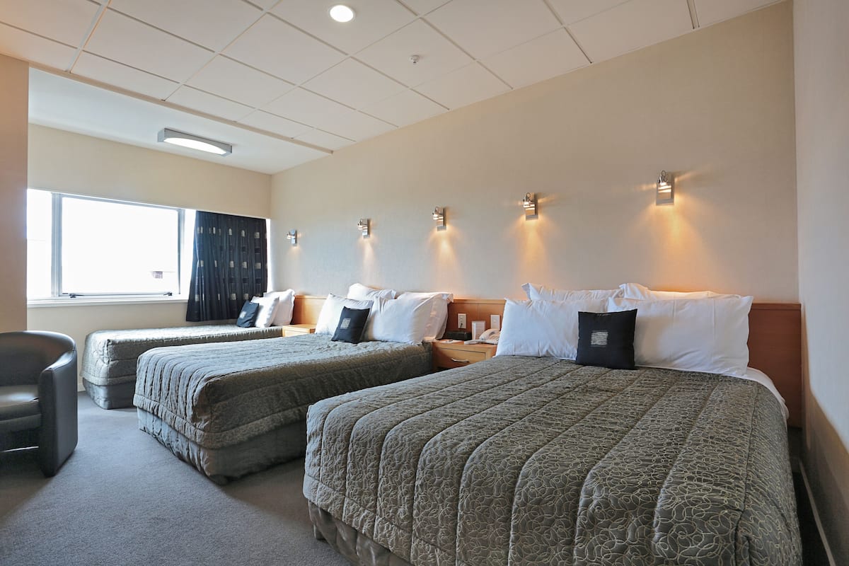 Quarto de hotel com duas camas, uma cadeira, uma escrivaninha e uma janela com cortinas.