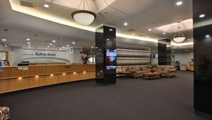 Un espace d’accueil d’hôtel comprenant un comptoir de réception, un coin salon avec des canapés et un grand écran affichant des informations.