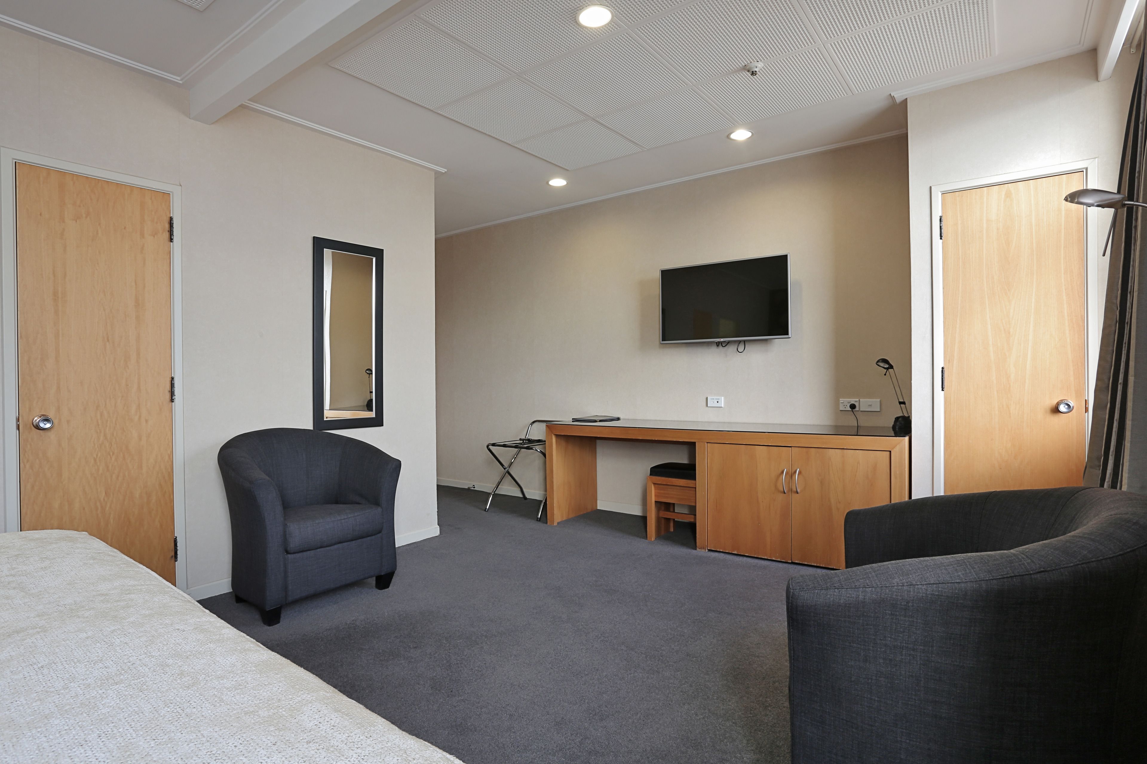 A hotel room with a bed, two armchairs, a desk, a television, and a mirror.