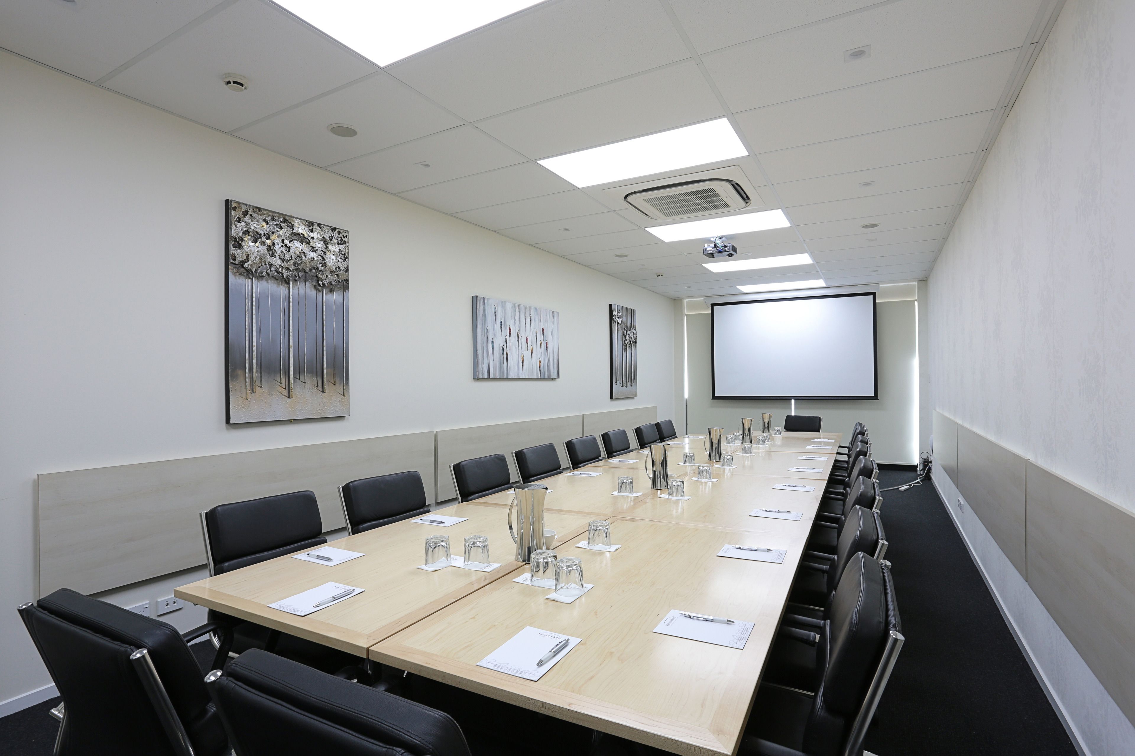 A conference room with a long table, black chairs, and a projector screen.