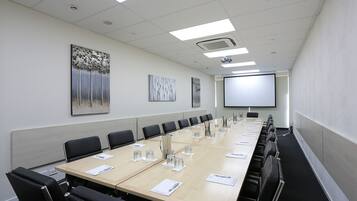 A conference room with a long table, black chairs, and a projector screen.