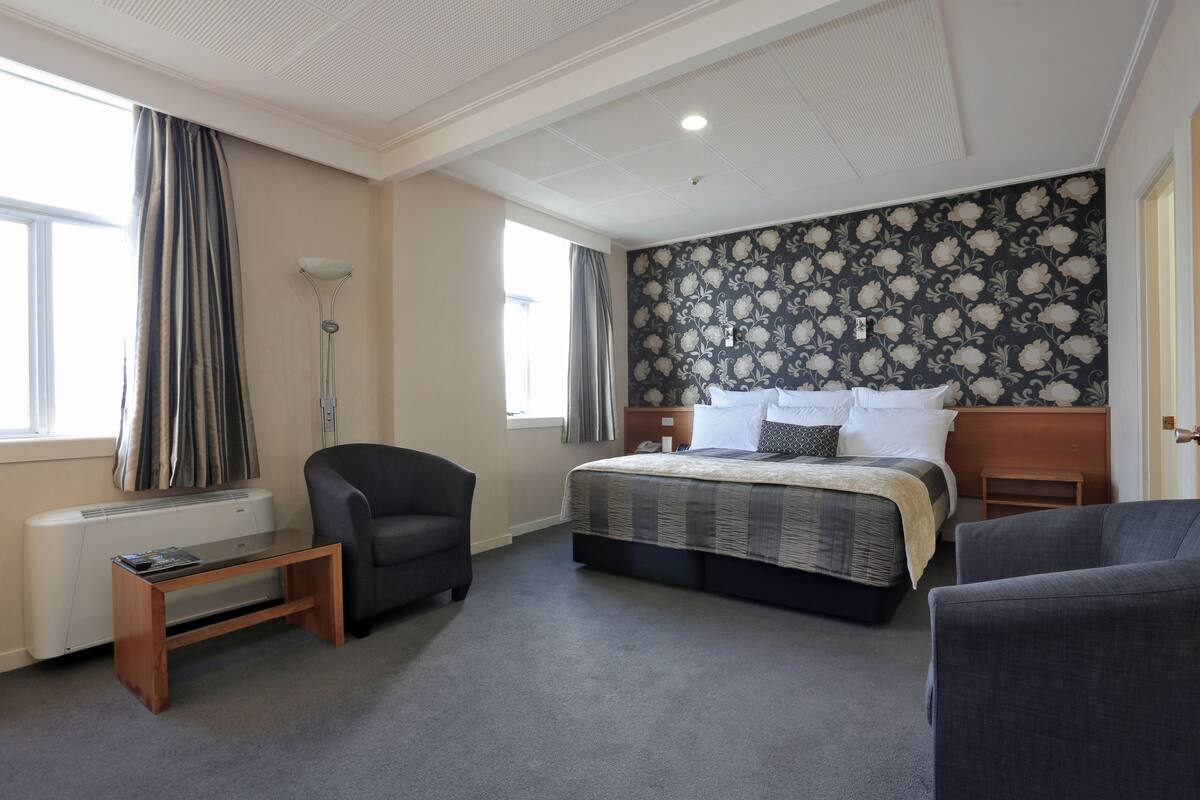 Quarto de hotel com uma cama grande, uma escrivaninha, uma cadeira e um radiador.