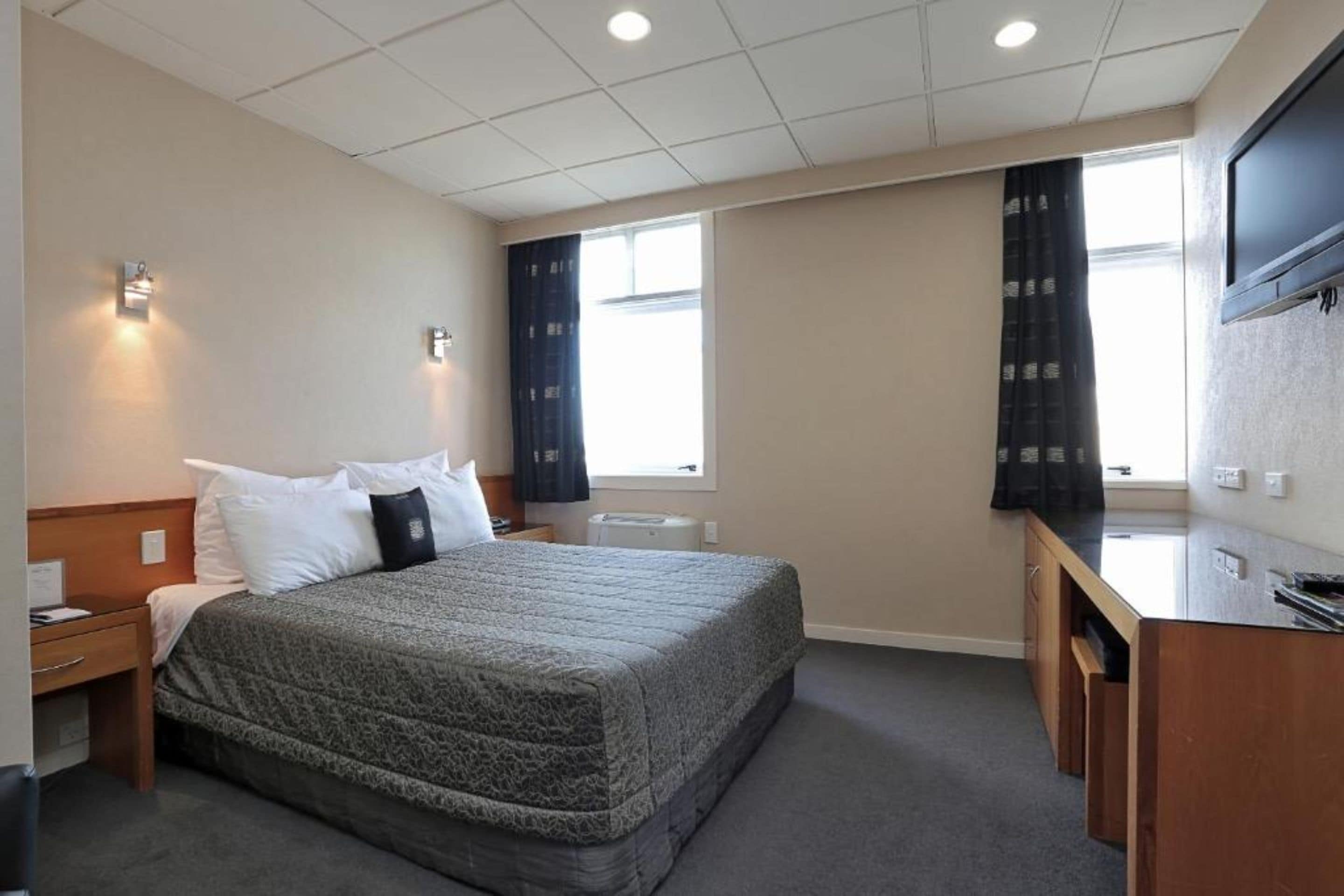 Une chambre d’hôtel équipée d’un lit, d’une table de chevet, d’un bureau et d’un téléviseur fixé au mur.