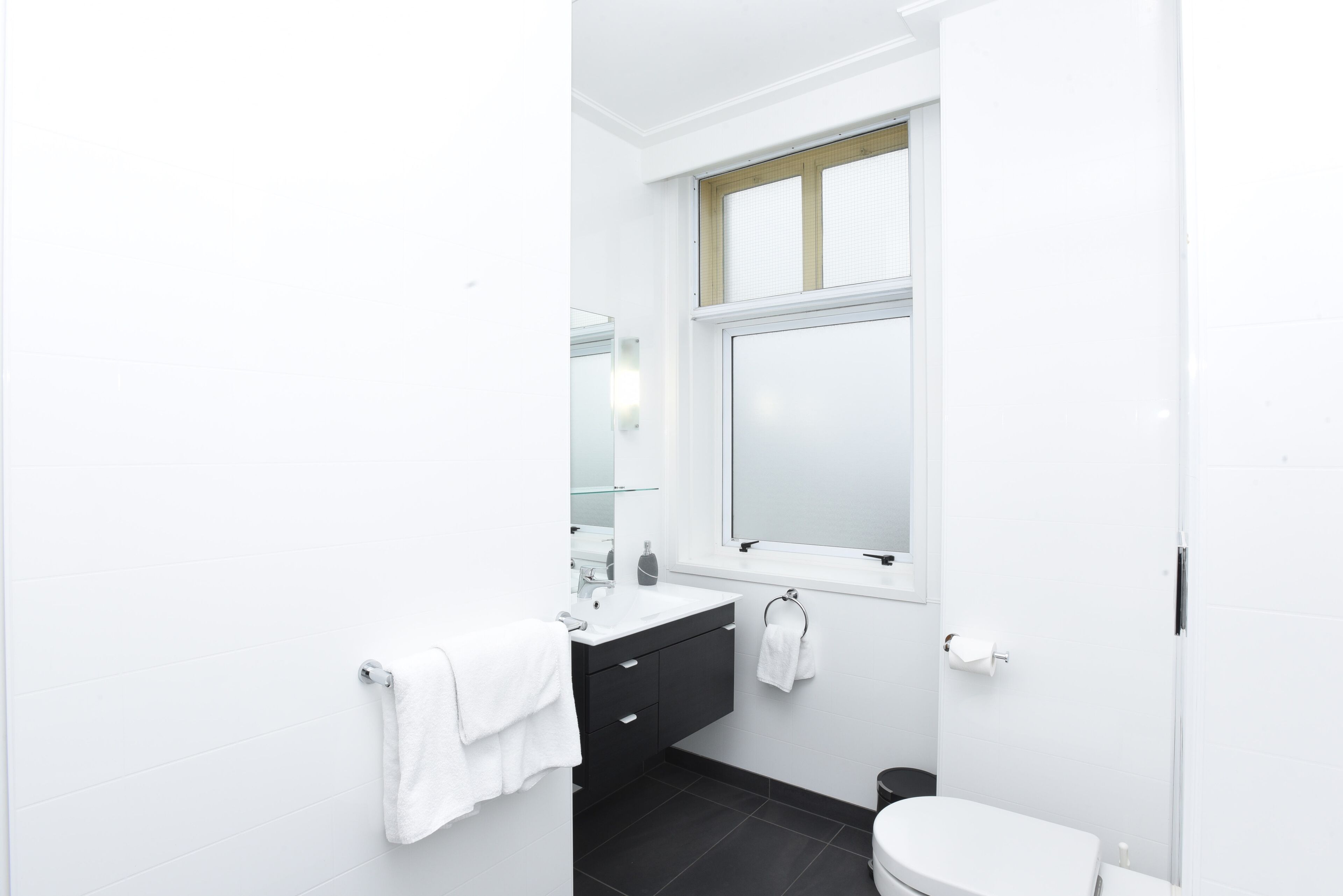 A modern bathroom with a white sink, black vanity, and a toilet.