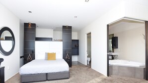Une chambre à coucher moderne avec un grand lit, des étagères intégrées, un grand miroir rond et une salle de bain séparée avec une baignoire.